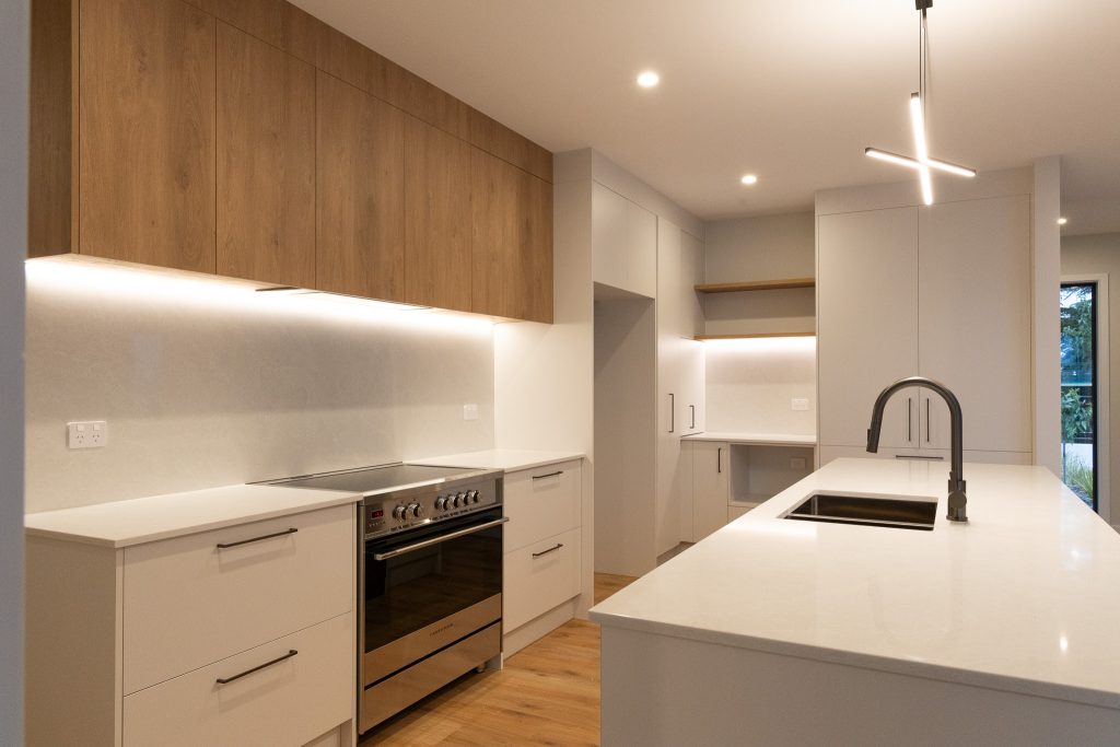 Contemporary kitchen featuring a timber island with vertical slats, white cabinets, integrated cooktop, and wood floors.